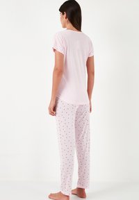 Light pink pajama set featuring a short-sleeve top and long pants. Pants have a small red heart print. Soft, smooth fabric with a relaxed fit.