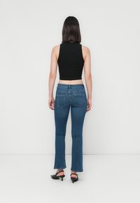 Svart avkortet tanktopp sammen med blå flarejeans med baklommer og subtil falming, komplementert av svarte hælsandaler.