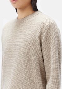 Beiger strukturierter Strickpullover mit Rundhalsausschnitt und langen Ärmeln, der ein dezentes Waffelmuster aufweist. Weiches, warmes Material.