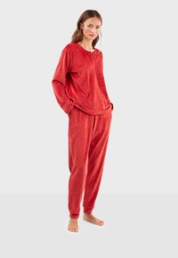 Ensemble de pyjama en velours rouge, top à manches longues avec col rond et motifs décoratifs, associé à un pantalon à taille élastique. Texture douce.