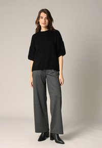 Pull en tricot noir et fluffy à manches courtes, associé à un pantalon gris à rayures bien taille haute et des bottines noires à talons pointus.