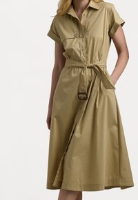 Khaki shirt dress with short rolled sleeves, a button-down front, a cinched waist secured by a belt, and a flared, mid-length skirt.