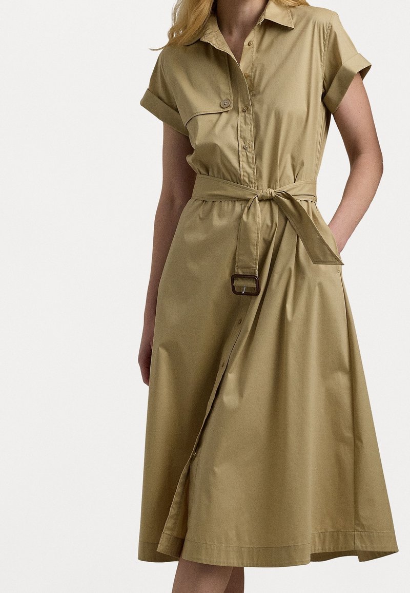 Khaki shirt dress with short rolled sleeves, a button-down front, a cinched waist secured by a belt, and a flared, mid-length skirt.