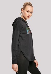Sudadera negra con dobladillo redondeado, que presenta letras gráficas vibrantes en la parte frontal. Hecha de un tejido suave, tiene un corte relajado y capucha con cordón.