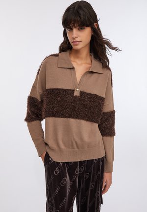 Maglione marrone con collo a polo, caratterizzato da strisce pelose di colore marrone scuro, polsini a costine e un piccolo dettaglio di cerniera dorata. Tessuto morbido.