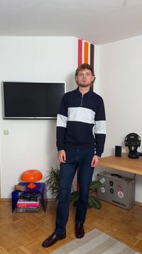 Marinblå och ljusgrå tröja med dragkedja och broderad text, kombinerad med mörka jeans och glänsande bruna skor, poserad inomhus.