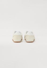 Hellebeige Wildleder-Sneaker mit weißen Akzenten, runder Form, Gummisohlen und einem schlichten Design. Glatte Textur im Obermaterial.