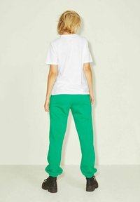 Camiseta de algodón blanca combinada con pantalones de chándal verdes. Los pantalones cuentan con una cintura y puños elásticos. Botas gruesas negras completan el conjunto.