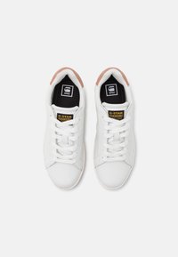 Witte sneakers met een glad leren bovenwerk, ronde neus en platte veters. Zwarte binnenzolen en lichtroze accenten op de hak. G-Star logo zichtbaar.