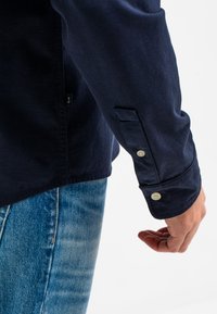 Donkerblauwe button-up shirt met een gladde stoftextuur, lange mouwen en knoopmanchetten, gecombineerd met lichtblauwe denim jeans.