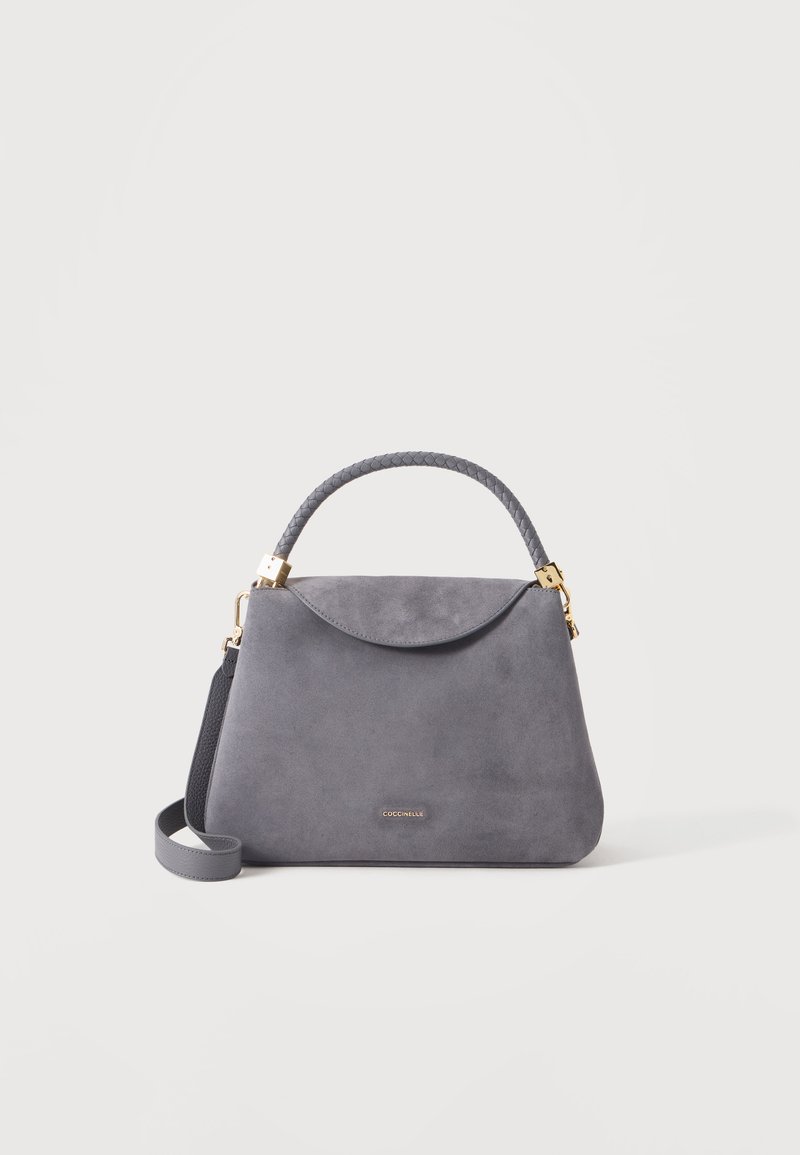 Sac à main en daim gris avec poignée tressée, ferrures dorées et bandoulière amovible sur fond blanc.