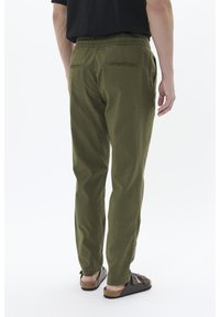 Pantaloni verdi dalla vestibilità comoda, con vita elastica, due tasche posteriori e gambe affusolate, abbinati a sandali scuri con suola in sughero.