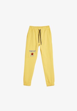 Pantalons de survêtement jaunes avec une taille élastique et un cordon noir, arborant le texte "TIME-OUT" et un graphique de basket-ball sur la jambe gauche.