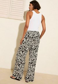 Mustvalge mustriga laiad püksid lillemotiiviga, kantud koos valge tank-topsiga, elastse vöökoha ja madala kontsaga sandaalidega.