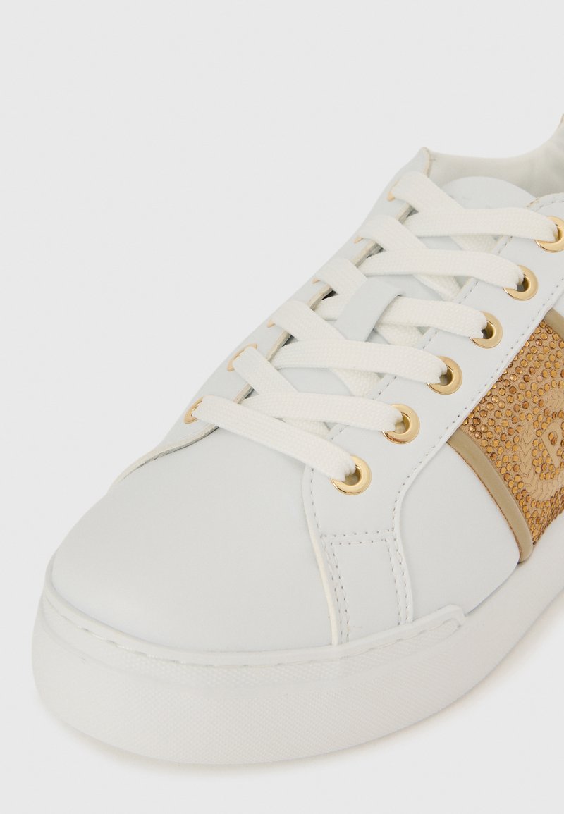 Sneaker in pelle bianca con occhielli dorati, accenti in pelle scamosciata marrone chiaro, lacci piatti e suola in gomma. Vista ravvicinata che mette a fuoco i dettagli superiori.