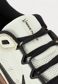 Nike sneaker featuring a white mesh upper, black laces, and a textured outsole. Includes a label with the brand name and product details.
