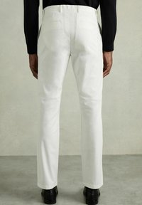 Pantaloni albi cu un design drept, cu două buzunare spate și o textură netedă din bumbac. Purtați cu pantofi negri.