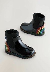 Svarta blanka anklar stövlar med elastiska ribbade sidor och regnbågsrandiga mockadetaljer på hälen. Har en texturerad sula och flerfärgad söm.