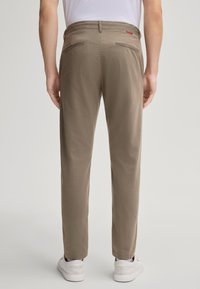 Khaki broek met een slim fit, voorzien van twee achterzakken en een zachte textuur, gecombineerd met witte sneakers.