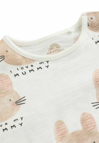 Camiseta de tela blanca con estampados de conejitos color marrón claro y texto "Amo a mi MAMÁ". Presenta un escote redondo y un cierre a presión en el hombro.
