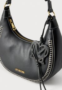 Μαύρη δερμάτινη τσάντα ώμου με χρυσά μεταλλικά στοιχεία, κλείσιμο με φερμουάρ, λευκά ραφές και διακοσμητική καρδιά με το γράμμα «Μ».