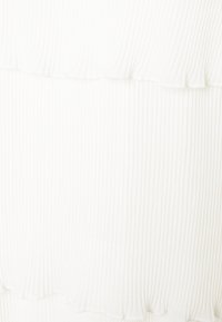 Detalhe do vestido branco com babados, apresentando uma textura estriada vertical, bordas suaves e um tecido leve e suave.