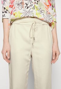 Lichtbeige joggerbroeken met een elastische tailleband en trekkoord. Heeft zijzakken en een gladde, licht matte textuur.