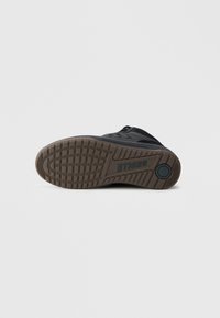 Crna sportska cipela s gumenim potplatom koji ima uzorak za bolje prianjanje. Na potplatu je vidljiv natpis "ETNIES". Minimalistički dizajn.