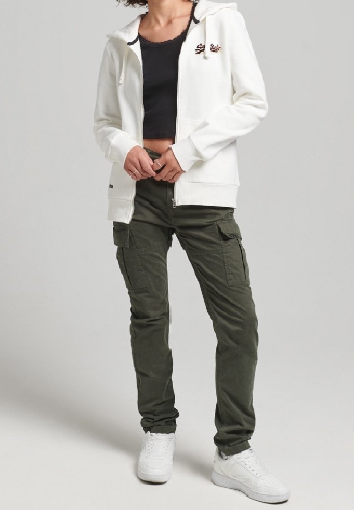 Sudadera blanca con cremallera y bolsillo frontal, top negro corto, pantalones cargo verde oliva con bolsillos laterales y zapatillas blancas.