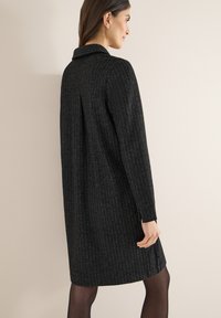 Vestito nero a motivo spina di pesce con maniche lunghe, collo e spacchi laterali, realizzato in tessuto strutturato, che arriva a metà coscia.