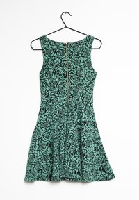 Robe florale verte avec un motif de roses noires, présentant un corsage ajusté et une jupe évasée, suspendue à un crochet noir sur fond blanc.