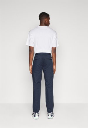 Pantalones azul marino de corte relajado, con cinturilla elástica y dos bolsillos traseros. Combinados con una camiseta blanca sencilla y zapatillas deportivas.