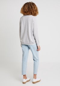 Grauer Strickpullover, hellblaue Jeans, weiße Turnschuhe mit hellbraunen Sohlen. Rückansicht mit weicher Textur und lockerer Passform.