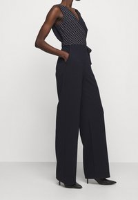 Laivaston haalari, jossa on tiukasti istuva, kuvioitu yläosa ja leveät lahkeet. Varustettu syvällä V-puolella, sivutaskuilla ja sileällä tekstuurilla.