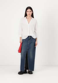 Camicia bianca in lino con maniche a tre quarti, abbinata a una lunga gonna di jeans con uno spacco frontale, completata da una borsa rossa.