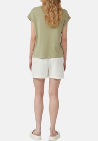 Olijfgroene T-shirt met korte mouwen van zacht materiaal, gecombineerd met witte textuurbroekjes. Het shirt heeft een relaxte pasvorm en opgerolde mouwen.