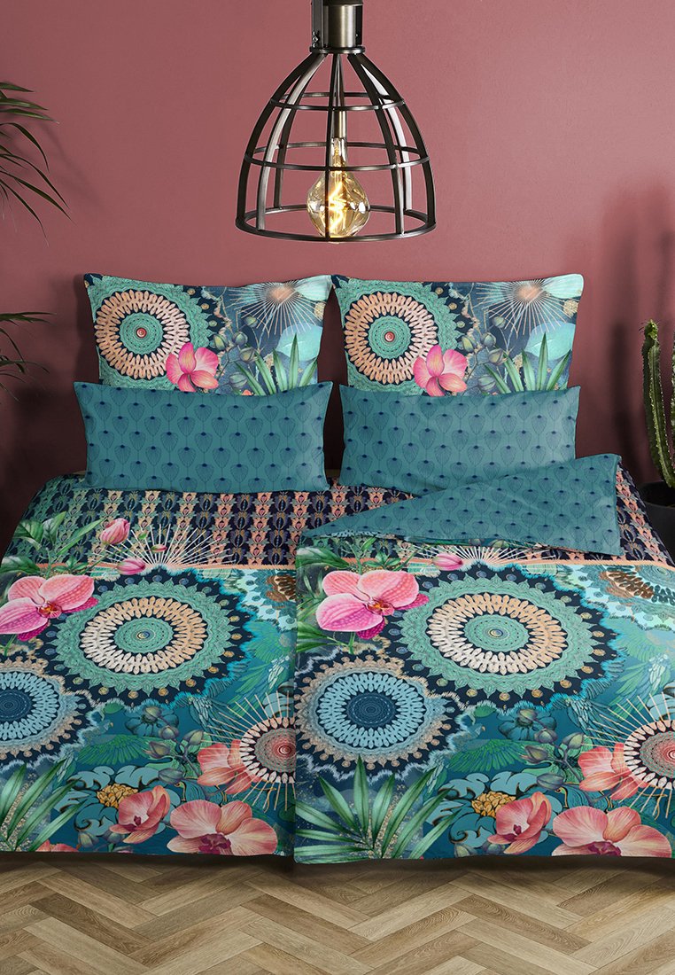 Doppelbett mit lebhaftem Blumen- und Kreisdesign-Bettzeug in Blau und Rosa, überragt von einer modernen Pendelleuchte in Form eines schwarzen Käfigs.