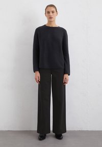 Schwarzer Pullover mit langen Ärmeln und Rundhalsausschnitt, kombiniert mit hoch taillierten, weit geschnittenen schwarzen Hosen. Glatte Textur, minimalistisches Design.