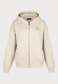 Sweat à capuche beige zippé avec poches avant, poignets et ourlet côtelés, et petit logo "Pegador" vert et jaune sur la poitrine gauche.