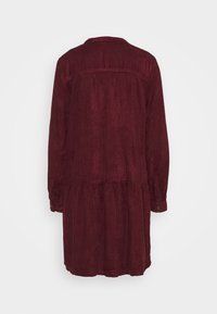 Robe en velours côtelé rouge foncé à manches longues, poignets boutonnés, taille froncée et col, vue de dos sur un fond uni.