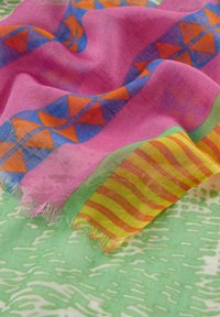 Écharpe légère avec une base rose décorée de motifs géométriques bleus et oranges, et un bord rayé vert et jaune. Texture douce.