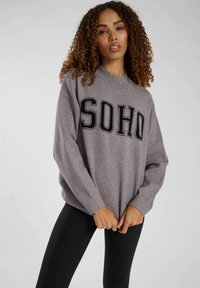 Grå sweatshirt med "SOHO" tryckt i fet svarta bokstäver. Har en avslappnad passform, rundad hals och ribbade ärmslut. Matchas med svarta leggings.