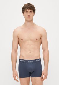 Boxer briefs para homem em azul-marinho, com um design liso, feitos de um tecido suave, com uma cintura elástica branca com marca.