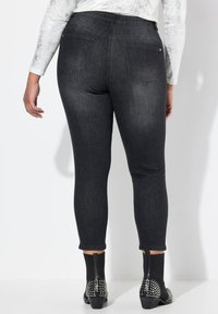 Jeans skinny de mezclilla negra con cintura alta, bolsillos traseros y una textura suave, combinados con botines con acentos de tachuelas.