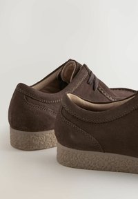 Brune ruskindssko med en struktureret beige sål, med minimal snøring og blødt indvendigt for. Glat finish med diskrete syninger.