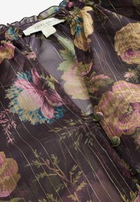 Peršviečiamas gėlėmis margintas bluzonas su violetiniu fonu, kuriame yra daugiaspalvių gėlių, auksinių juostelių ir apvalių audiniu padengtų sagų.