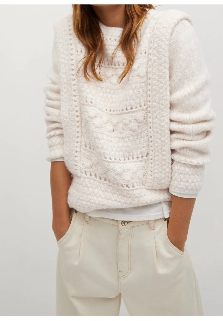 Pull en tricot rose clair avec des motifs texturés, encolure ronde et manches longues, associé à une couche blanche en dessous et un pantalon couleur crème.