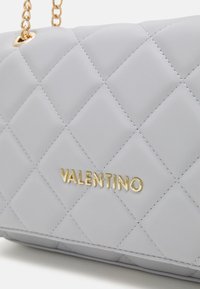 Prošívaná šedá kožená kabelka se zlatým logem a řetízkovým popruhem, s hladkým povrchem a diamantovým vzorem na celé ploše.