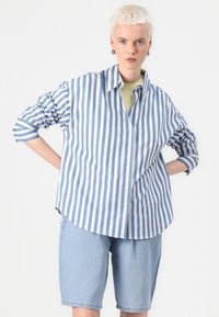 Button-up shirt with blue and white vertical stripes, long sleeves rolled up, paired with light blue denim shorts.