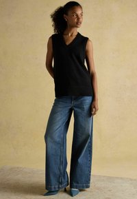 Czarny bezrękawnik dzianinowy z dekoltem w serek, w zestawieniu z szerokimi niebieskimi dżinsami i niebieskimi czółenkami na szpilce. Prosty fason i miękka faktura.